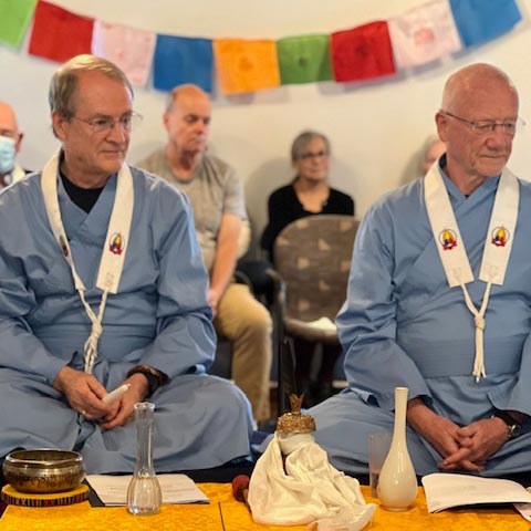 retreats-community A group of men sitting and standing together in an outdoor wooded area, dressed casually, smiling and posing for a group photo.